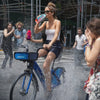 Woman riding thru a puddle of water in the city streets while drinking a bottle of guavalicious 